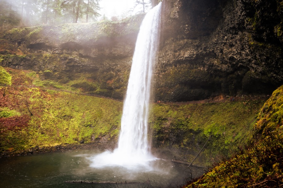 A tall waterfall drops over a moss-covered cliff into a pool.